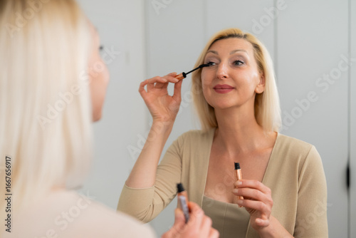 Stylish lady applying volumizing mascara to upper lashes for dramatic look