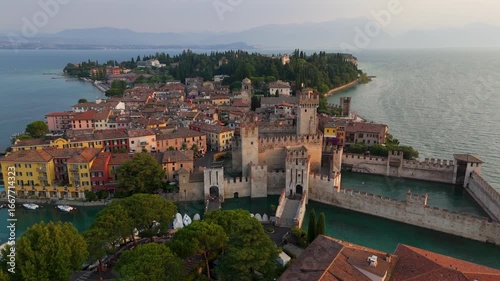 Aerial drone wide shot of Castello Scaligero di Sirmione castle and Sirmione town on Lake Garda, Italy, at summer sunrise.
