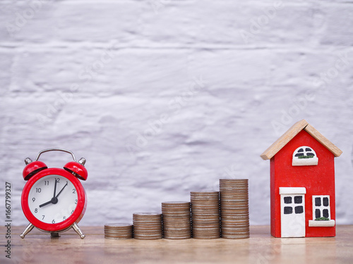 Miniature house, Read alarm clock and stack of coins. The concept of saving money and and manage time for house, Property investment, House mortgage, Real estate in the future
