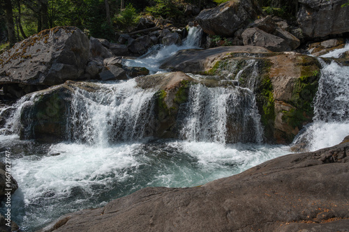 A mesmerizing cascade flows over smooth rocks, framed by lush green trees in the Pyrenees, capturing the tranquil essence of the environment near Pont d'Espagne.