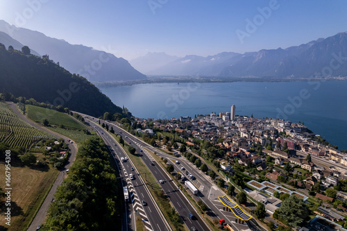 Lake Geneva in Switzerland seen from above with French Alps in the background on a sunny hazy day and Montreux cityscape below the freeway in the foreground