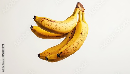 Bunch of yellow bananas, speckled with brown spots, suspended in mid-air against a plain white background