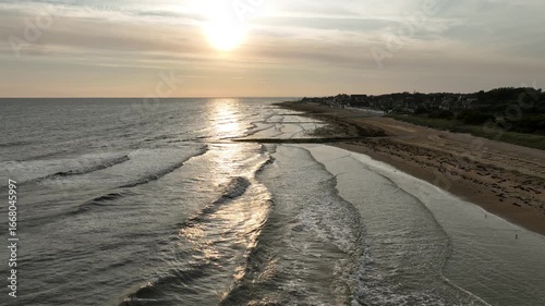 Aerial view of the serene coastline where the ocean meets the sandy beach in Bernières-sur-Mer, Normandy, France.
