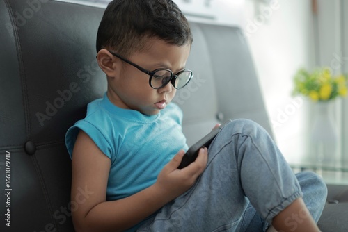 Child using smartphone on sofa in house, children holding phone 