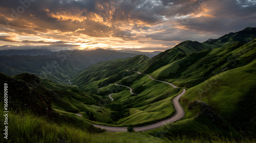 Picturesque winding road in green mountains under colorful golden sunset clouds wide scenic panorama