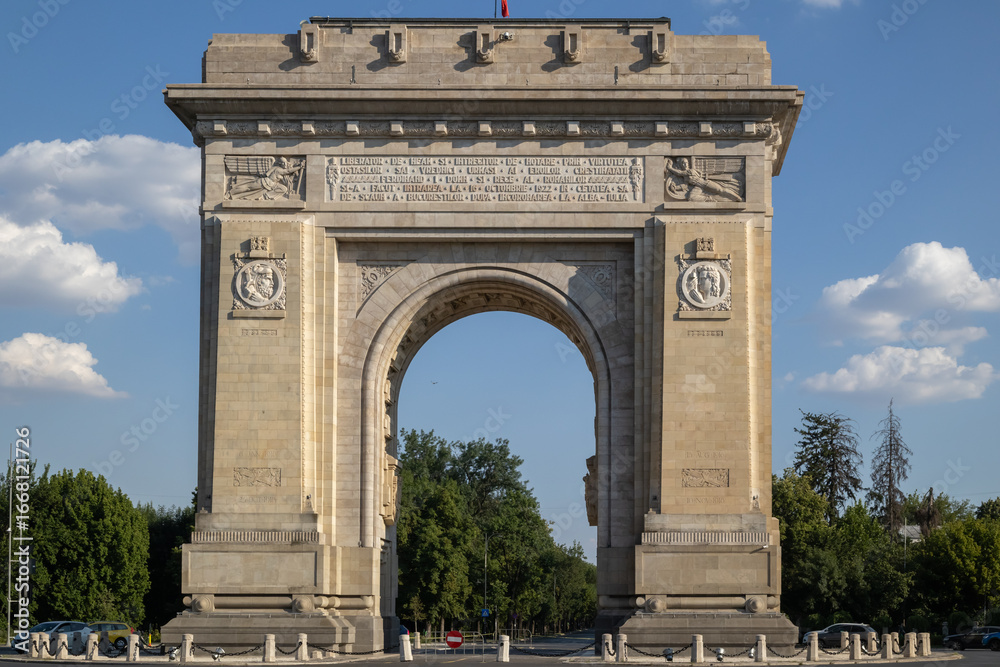 Obraz premium The Arcul de Triumf stands proudly on a sunny day in Bucharest, Romania. This historic arch honors Romanian soldiers of World War I