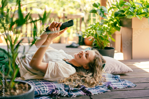 Bild auf Leinwand Beautiful young woman with a mobile phone in her hands lying on the summer terra