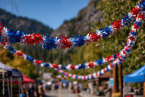 Fototapeta Naklejka Na Ścianę i Meble -  Garlands of red, white and red flowers are hung on the streets of a small picturesque town. Street festival in the city, decorations.