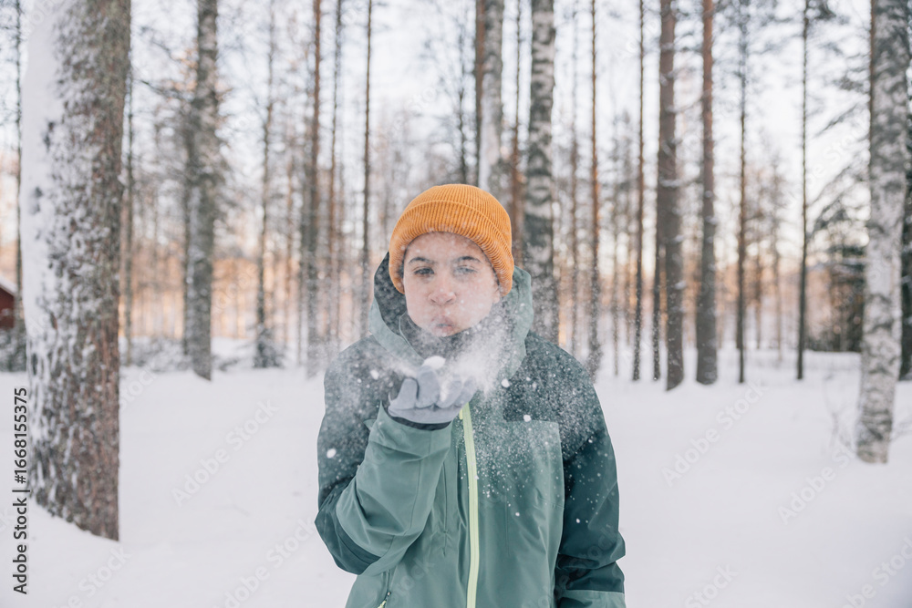 Fototapeta premium Young girl blowing snow in a winter forest
