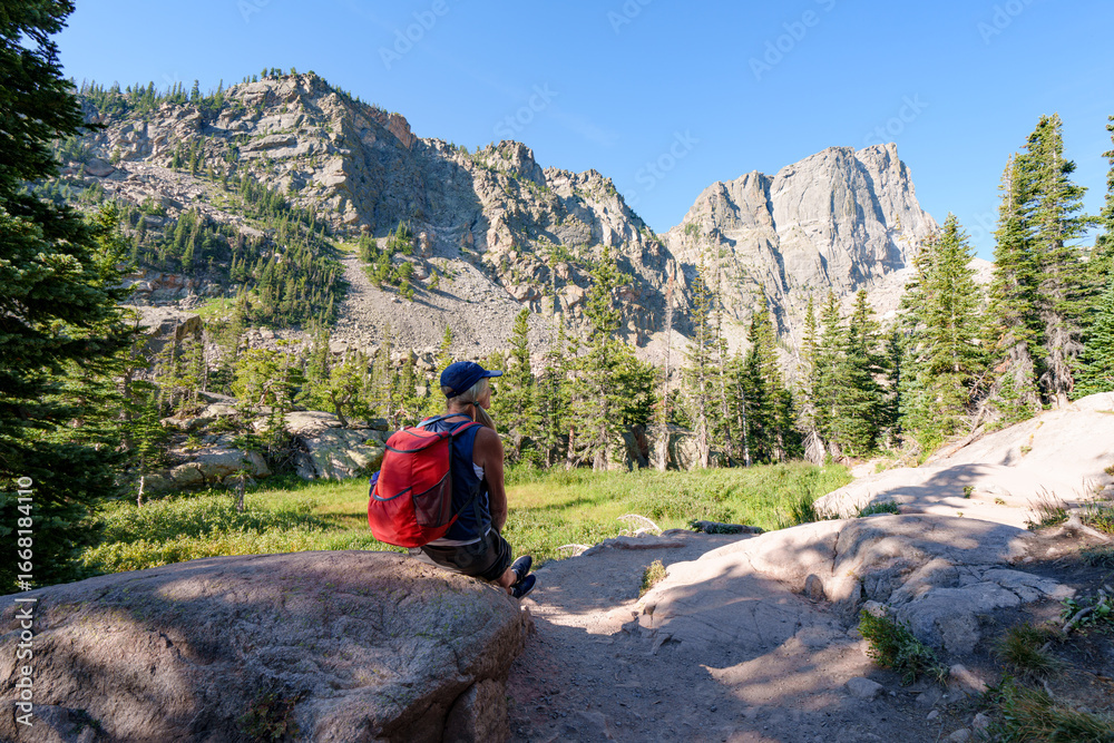 Fototapeta premium Woman hiker sitting on rock and viewing the mountains; hiking in the Colorado Rocky Mountains.