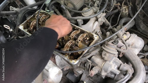 mechanic is conducting a manual tune-up on the rocker arm assembly of a car engine.