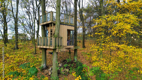 Quadro su tela A small wooden treehouse built among tall trees in an autumn forest, with yellow leaves surrounding it