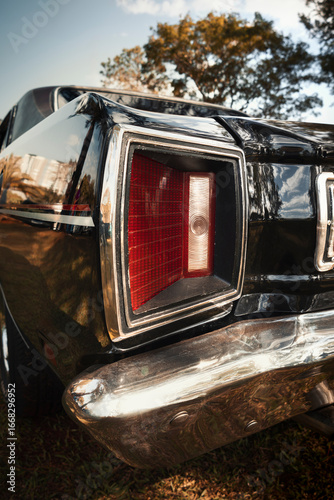 Rectangular taillight with chrome frame on a classic car with black paint and polished steel bumper.
