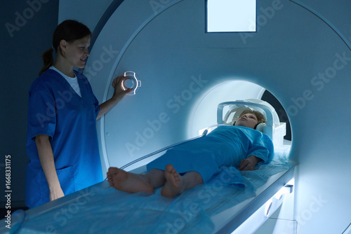 Obraz na plátne Caucasian middle aged woman operating MRI scanner while Caucasian child lying on