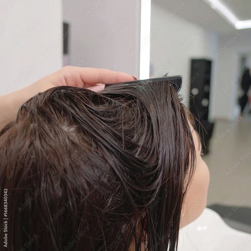 Fototapeta premium A person's wet dark brown hair is being combed by a hand in a salon setting.