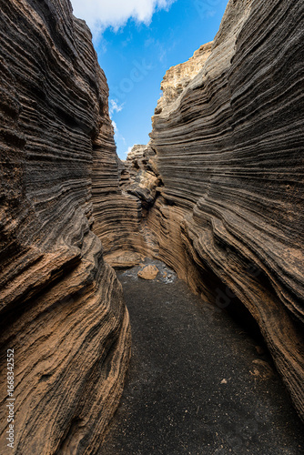 Narrow canyon showing layers of volcanic rock formations under blue sky
