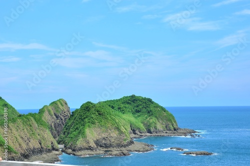 A beautiful coastal landscape at Bedil Island, Banyuwangi, Indonesia. Lush green hills covered in dense vegetation rise dramatically from the clear blue ocean