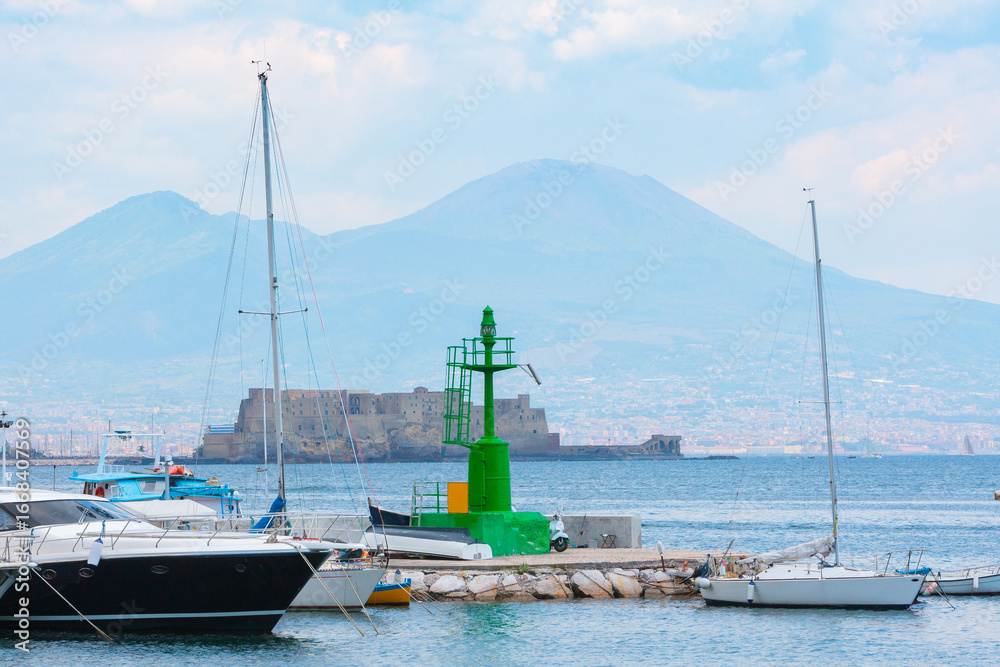 Fototapeta premium View from Molo di sopraflutto Sannazzaro also called Molo Luise marina in Naples, Italy. Yachts and other boats are moored in the harbor, with the cityscape and Mount Vesuvius
