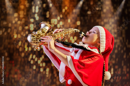 Girl child in red Christmas Santa hat playing saxophone in decorated hall.