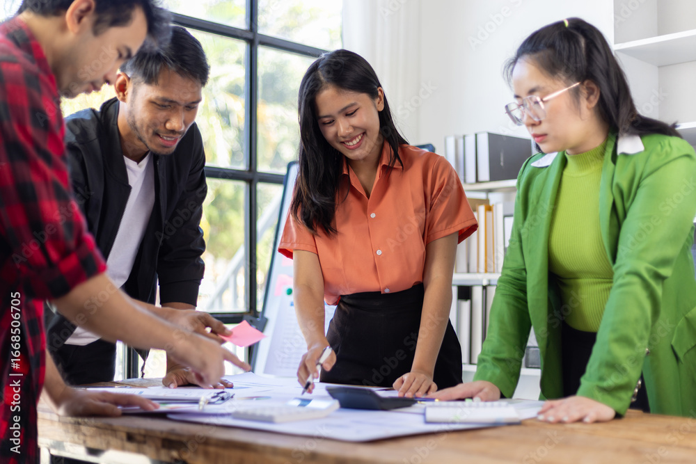 Fototapeta premium Startup business team analyzing documents at meeting table. Young entrepreneurs are reviewing documents and discussing business strategy during a meeting in a modern office space.