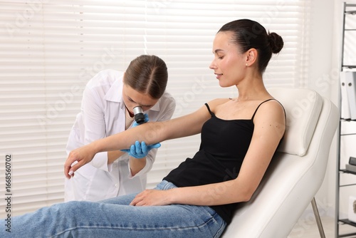 Doctor examining young woman's mole with dermatoscope in hospital