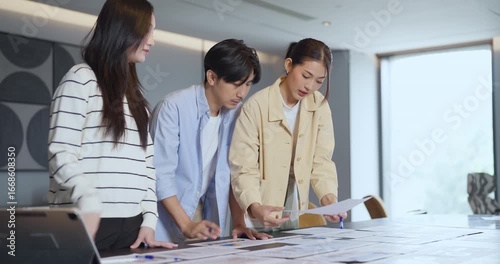 Three young business people discussing report and financial charts during office meeting, analyzing business data and planning marketing strategy for company teamwork success
