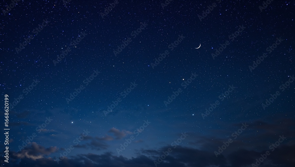 Fototapeta premium A crescent moon glows among countless stars within the deep blue night sky, featuring faint clouds near the horizon adding depth to the tranquil celestial scene