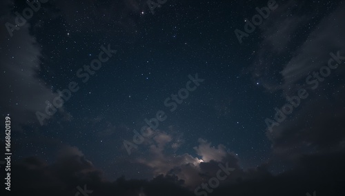 Starry night sky featuring drifting clouds illuminated faintly near the horizon, captured within the dark serene atmosphere with deep blue tones and a tranquil celestial view