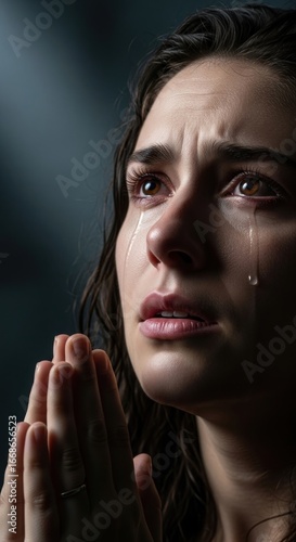 Emotional woman with tears praying in a dimly lit setting, conveying deep sorrow and hope