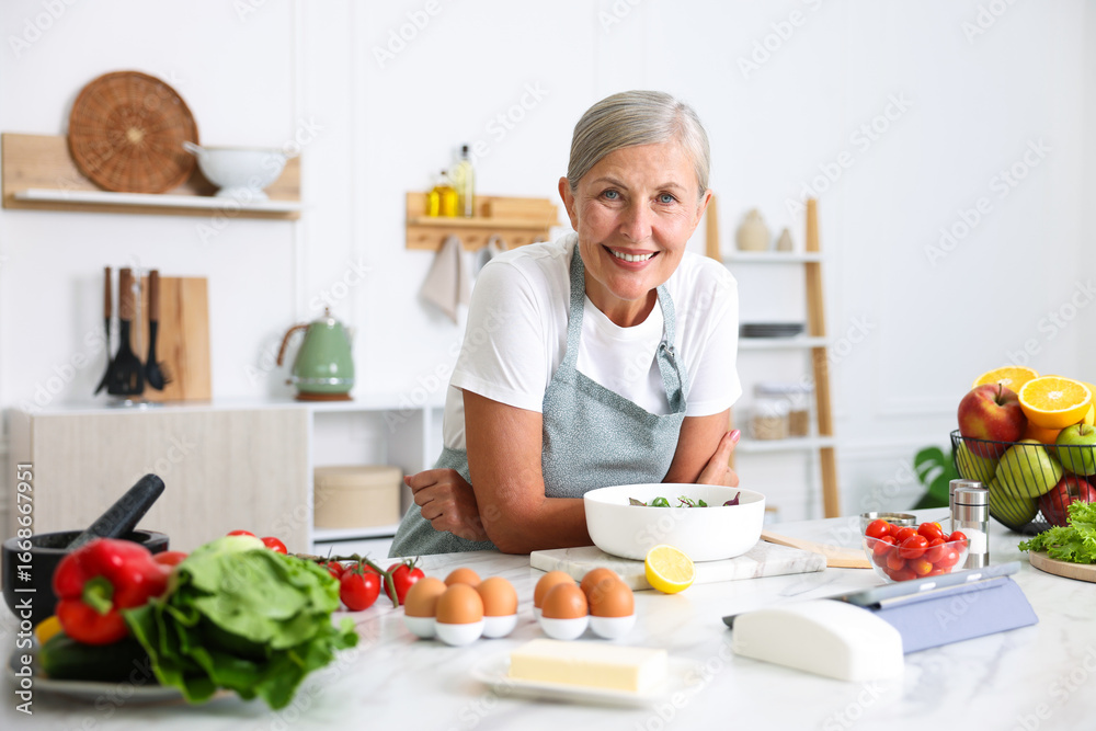 Senior woman cooking salad at white marble table in kitchen Senior woman cooking salad at white marble table in kitchen