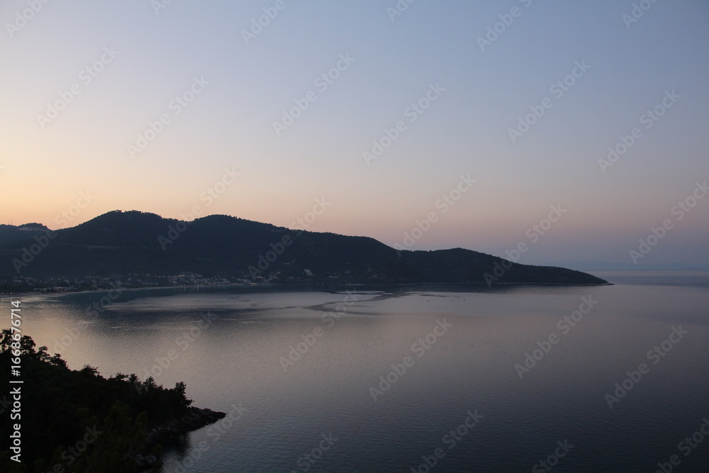 Obraz premium A wide-angle landscape of a bay or lake with a mountain in the background at dusk, showing a calm, serene body of water reflecting the soft light of the sky.