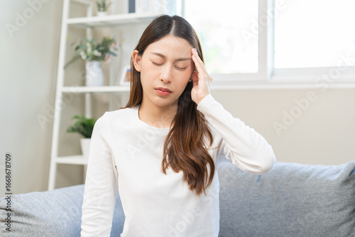 Free Download Dizzy asian young woman, girl headache or migraine pain suffering from vertigo while sitting on couch in living room at home, holding head with hand, health problem of brain or inner ear not balance. - GFXLoad