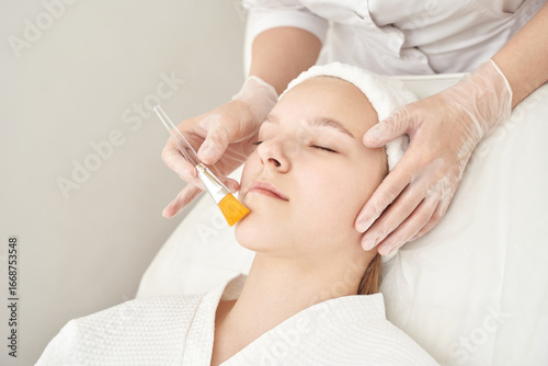 Young caucasian female receiving facial treatment at spa by gloved professional.