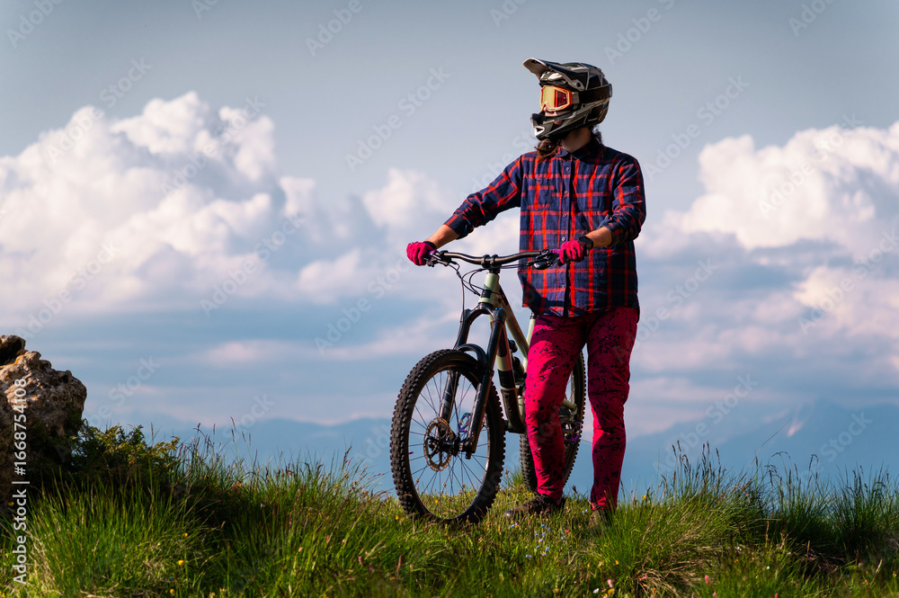 Naklejka premium Unrecognizable athlete in protective gear standing in a field and looking at the camera against the backdrop of foggy mountains and cumulus clouds. Mountain sports concept