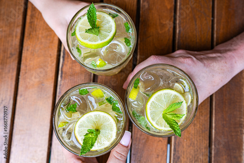 Overhead view of three people sitting at a table making a celebratory toast with mojitos