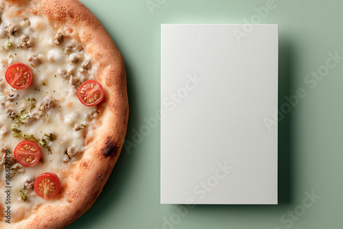 Fresh pizza with mozzarella, cherry tomatoes and herbs beside a blank white card on a pale green background.