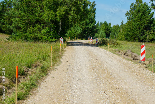 Obraz na plátně Gravel road under construction marked with stakes and warning signs in rural gre