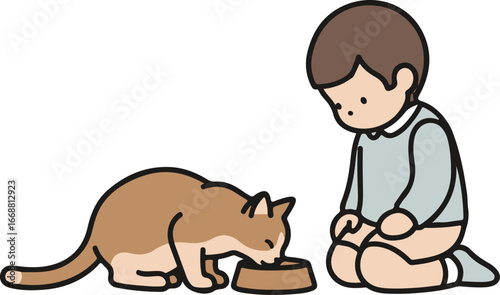 A gentle young boy in a blue shirt kneels and watches a brown cat eat from its bowl.