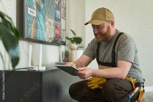Fotografie Caucasian middle aged man with beard wearing cap setting up wireless router usin