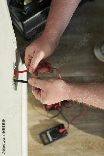 Wallpaper Mural Caucasian middle aged man using digital multimeter to test electrical wiring in wall socket, hands holding probes while measuring voltage, device resting on wooden floor Torontodigital.ca