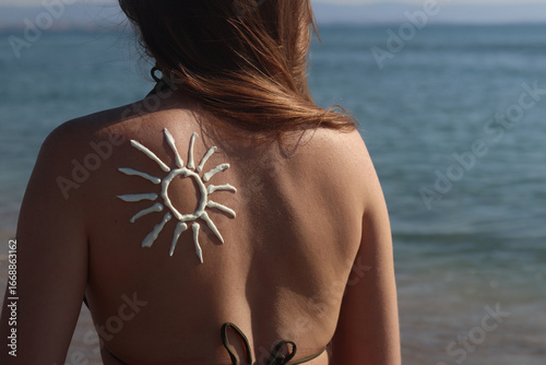 Sun image made with sunscreen on woman's back. Sunbathing on the beach. Close-up. Woman in swimsuit on the beach, back view. Using sunscreen. Concept of beach vacation, seaside resort, beach holiday