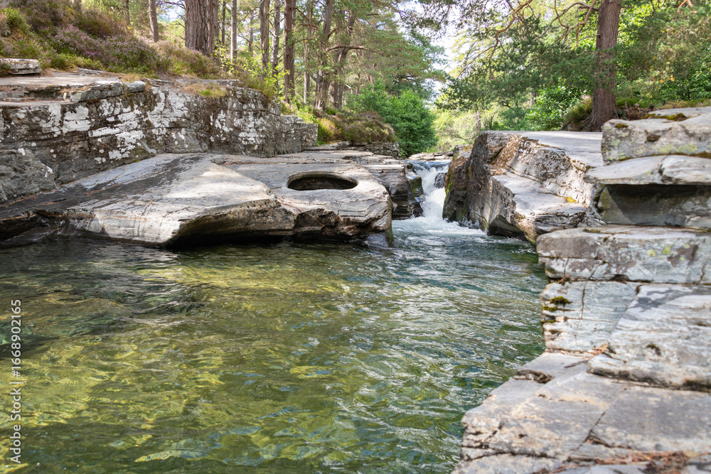 Naklejka premium A wide shot with long-exposure photo of the Linn of Quoich waterfall under Scots Pine trees.