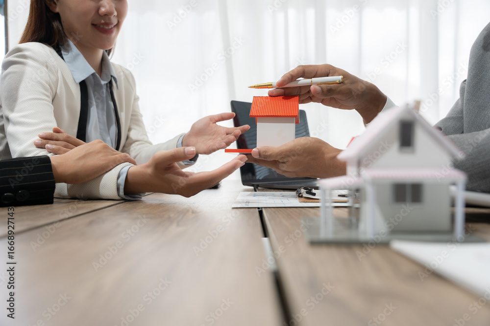 Fototapeta premium Real estate agent presenting a house model to client during a meeting, discussing property purchase terms and investment opportunities in a professional setting