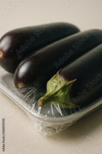 Fresh eggplants wrapped in plastic on tray