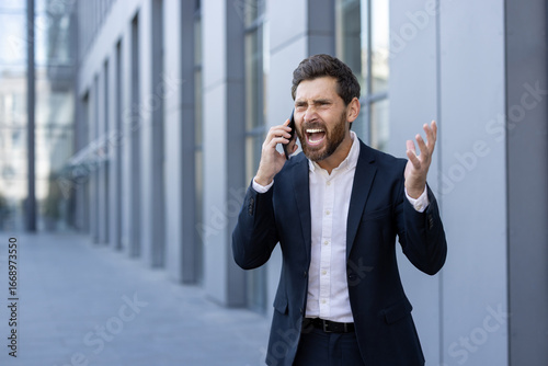 Фотография Businessman Expressing Anger During Phone Call Outside Modern Office Building