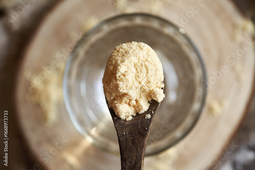 Whey protein powder on a wooden spoon above a cup of water