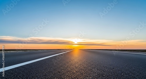 Empty asphalt road leading towards a bright sunset with a clear blue sky horizon