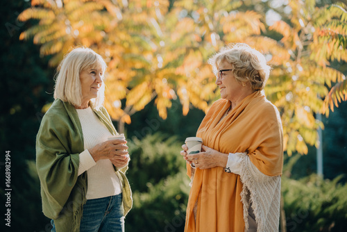Tableau sur toile Two senior women enjoying coffee and conversation in autumn park