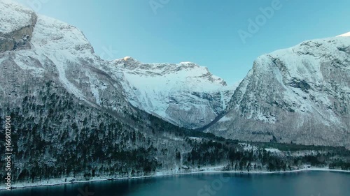 Wallpaper Mural aerial footage showcasing the serene winter landscape of a Norwegian fjord, possibly Eresfjord or Eikesdalen. Snow covered mountains rise dramatically from the tranquil waters, surrounded by a dense,  Torontodigital.ca