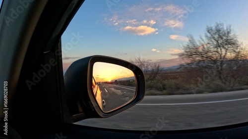 Sunset reflecting in car mirror during road trip. Warm sunset hues reflecting vividly on car side mirror, capturing expansive landscape and golden light during scenic road journey across countryside